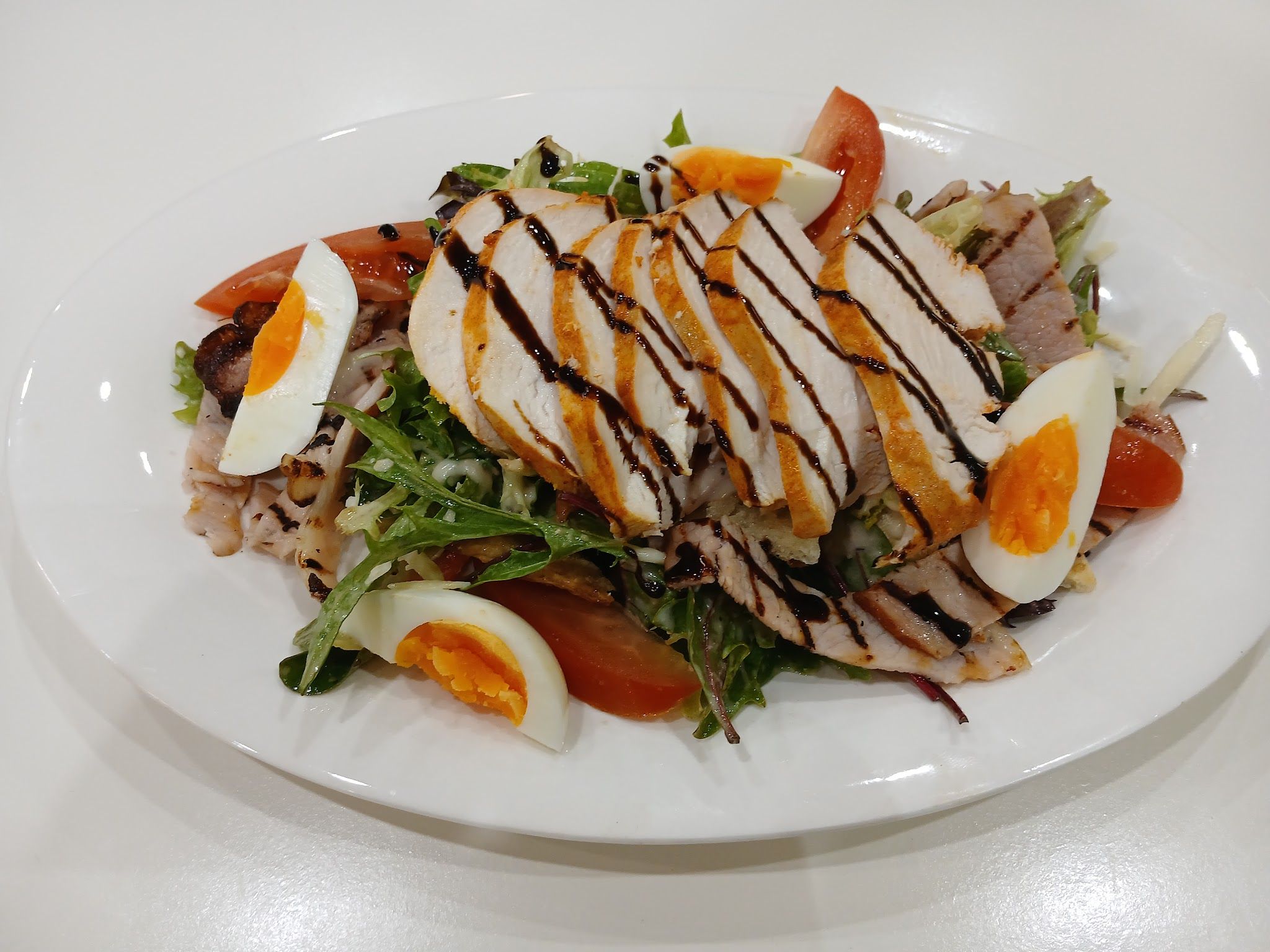 Grilled chicken salad with balsamic glaze, eggs and tomatoes on white platter