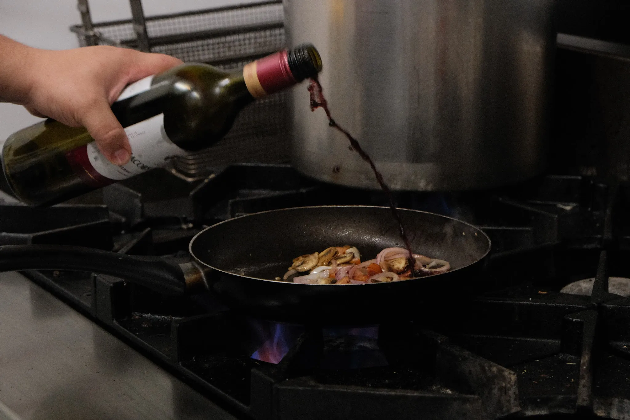 Chef pouring red wine into pan over gas flame in commercial kitchen