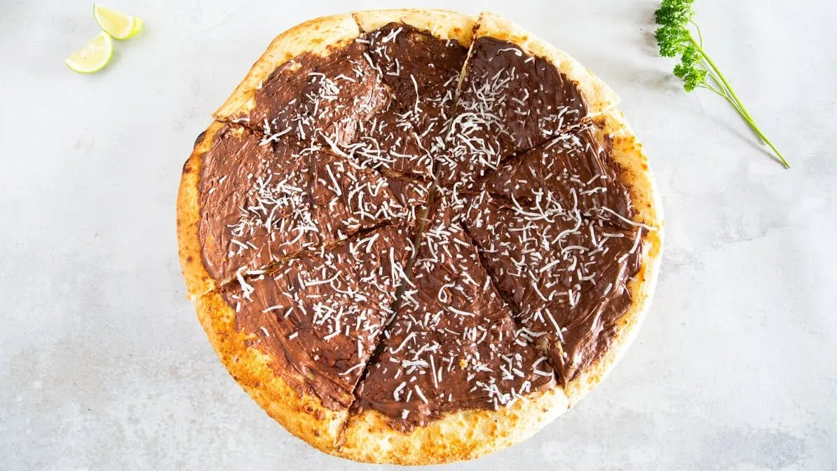 Nutella pizza with coconut shreds overhead on grey background