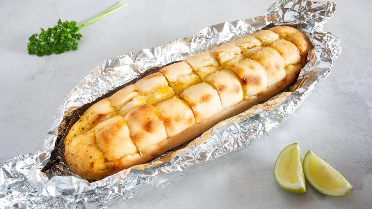 Cheesy garlic bread roll in foil on grey background with lime wedges