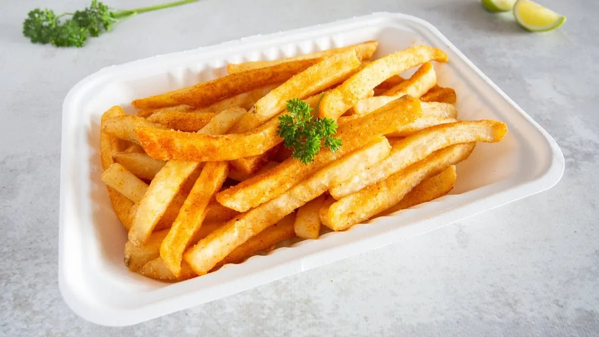 Seasoned crinkle-cut chips in white takeaway container on grey surface