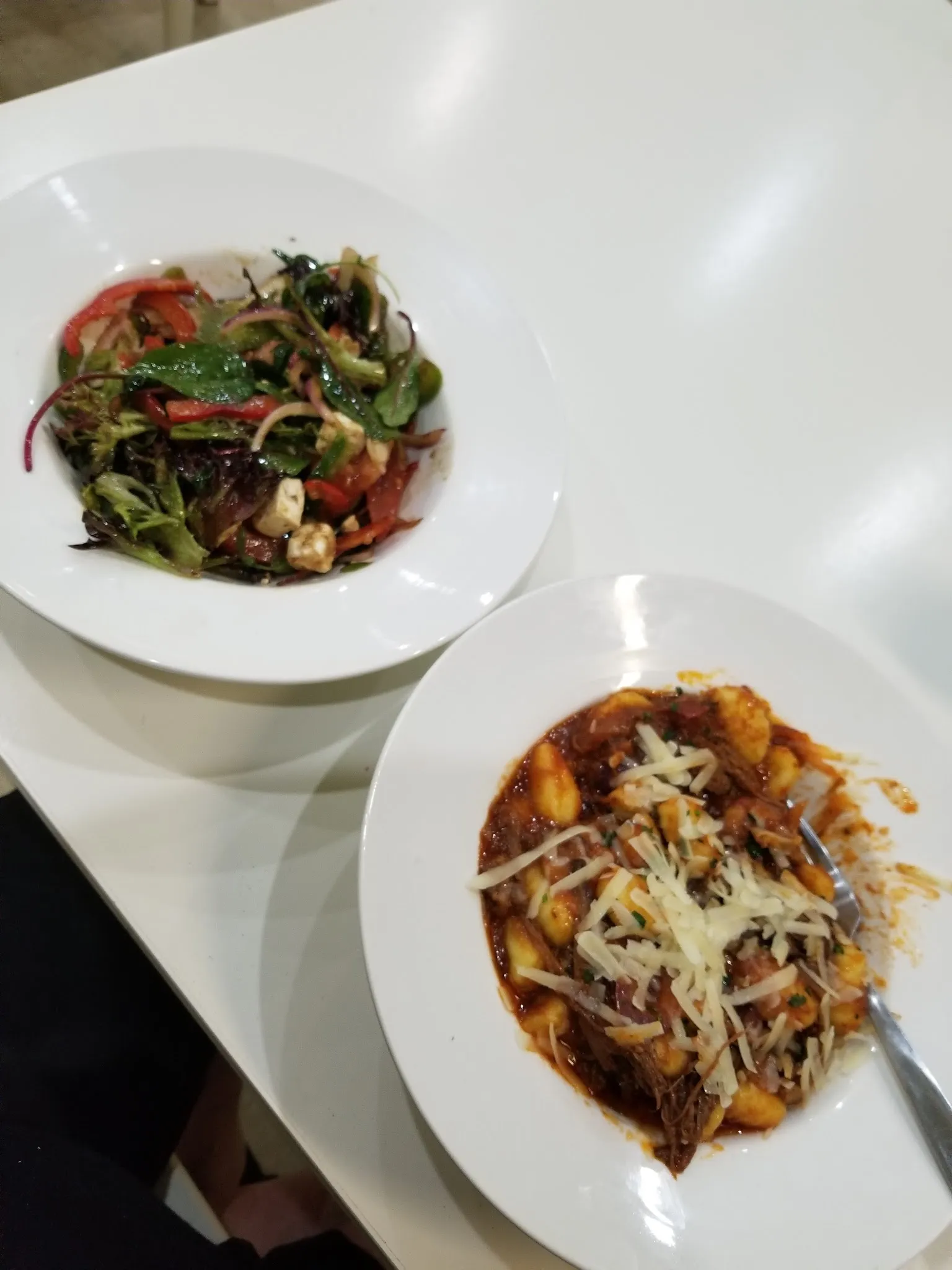 Greek salad and braised beef gnocchi served together on white table